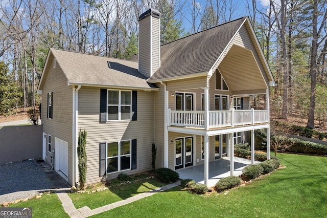 rear view of property with a chimney, a shingled roof, a patio, and a yard