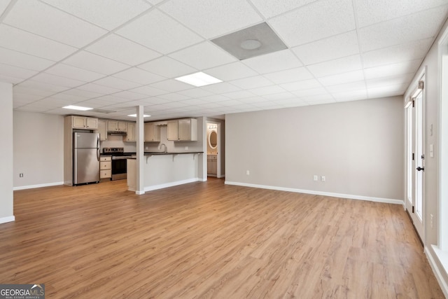 unfurnished living room with baseboards, light wood-style floors, a sink, and a drop ceiling