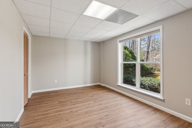 empty room featuring baseboards, light wood-style flooring, and a paneled ceiling