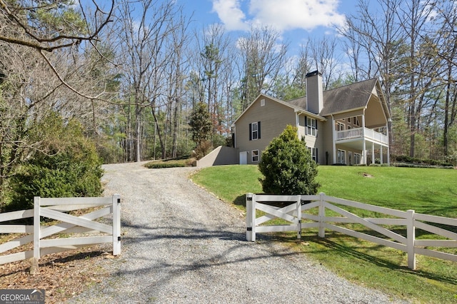 view of side of property featuring a balcony, a chimney, a fenced front yard, driveway, and a yard