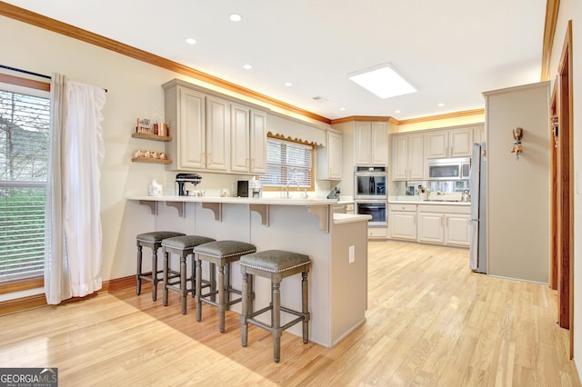 kitchen featuring a kitchen breakfast bar, appliances with stainless steel finishes, light wood finished floors, ornamental molding, and a peninsula