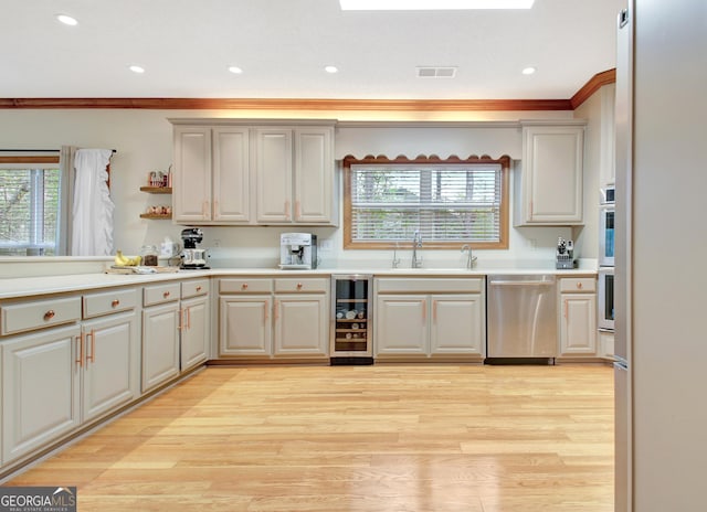 kitchen with beverage cooler, light wood-style flooring, appliances with stainless steel finishes, a sink, and visible vents