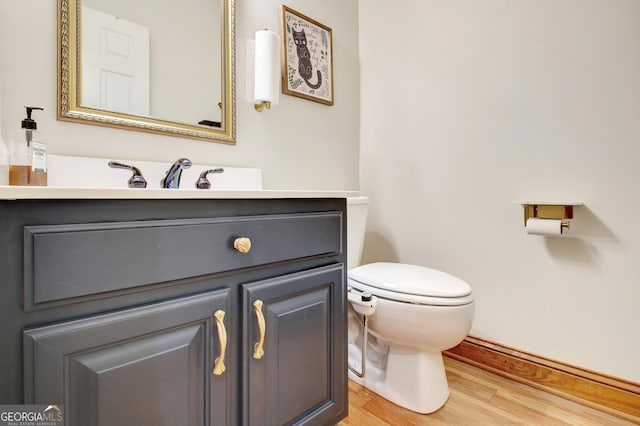 bathroom with toilet, vanity, wood finished floors, and baseboards