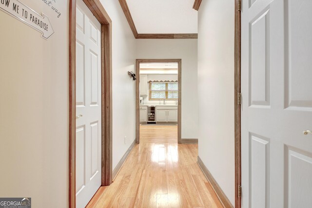 hall featuring ornamental molding, light wood finished floors, a sink, baseboards, and wine cooler