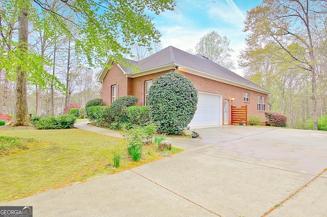view of side of home with a yard, brick siding, a garage, roof with shingles, and concrete driveway