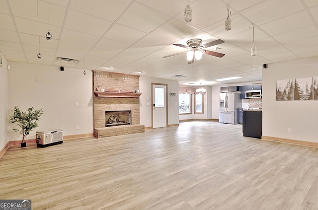 unfurnished living room with a drop ceiling, ceiling fan, a brick fireplace, light wood finished floors, and baseboards