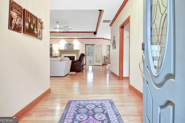 foyer entrance featuring a fireplace, light wood-style flooring, ceiling fan, and ornamental molding