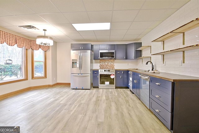 kitchen featuring open shelves, light wood-style flooring, stainless steel appliances, baseboards, and a notable chandelier