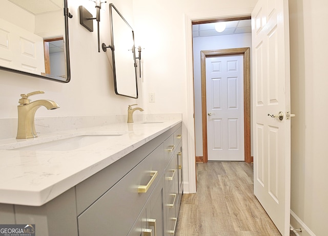 full bath featuring baseboards, wood finished floors, double vanity, and a sink