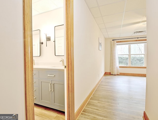 hall with a paneled ceiling, a sink, baseboards, and light wood-type flooring
