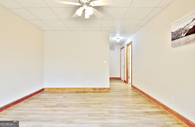 empty room featuring wood finished floors, a drop ceiling, baseboards, visible vents, and a ceiling fan