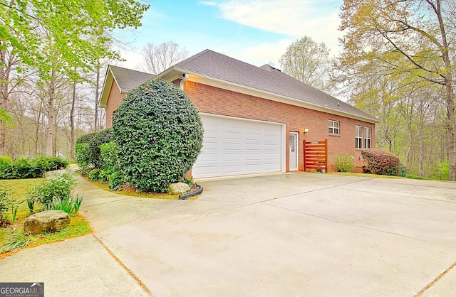 view of side of home with driveway, roof with shingles, an attached garage, and brick siding