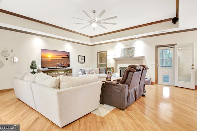 living room with ornamental molding, a ceiling fan, light wood-style floors, and a tray ceiling