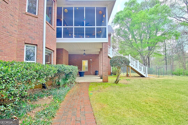 back of property featuring brick siding, stairway, a patio, a sunroom, and a lawn