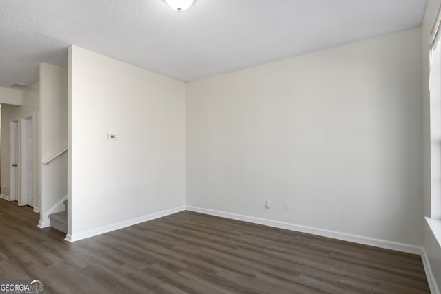 empty room featuring baseboards, dark wood-style flooring, and stairway
