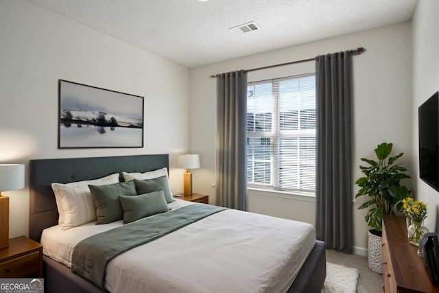 bedroom featuring light colored carpet, visible vents, multiple windows, and a textured ceiling
