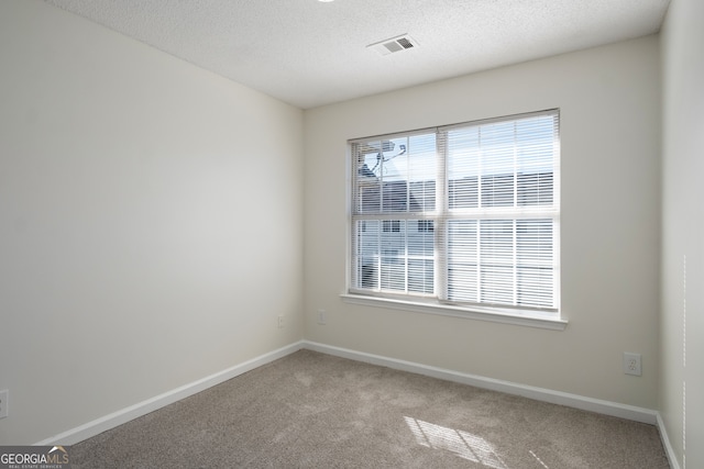 spare room with light colored carpet, visible vents, baseboards, and a textured ceiling