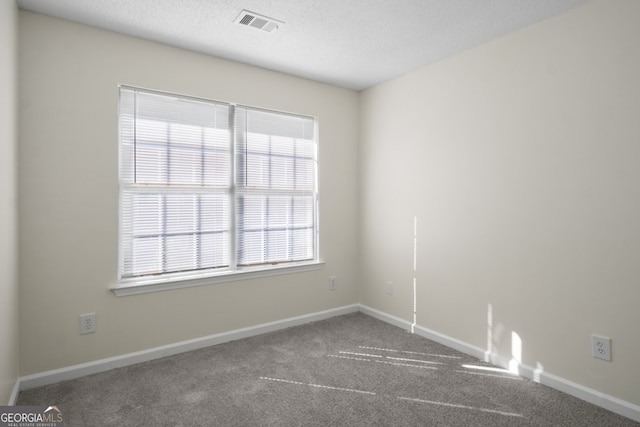 carpeted empty room featuring a textured ceiling, baseboards, and visible vents