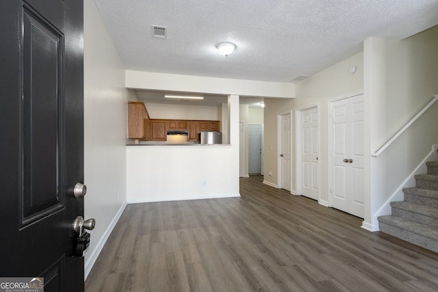 unfurnished living room featuring a textured ceiling, visible vents, baseboards, stairway, and dark wood-type flooring