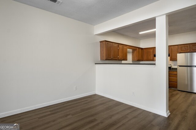 kitchen featuring freestanding refrigerator, a textured ceiling, dark wood finished floors, baseboards, and dark countertops