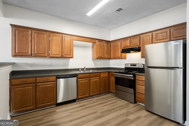 kitchen featuring brown cabinets, dark countertops, under cabinet range hood, and stainless steel appliances
