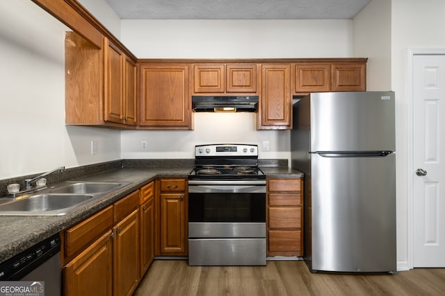 kitchen with a sink, dark countertops, under cabinet range hood, and appliances with stainless steel finishes