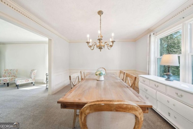 carpeted dining area with ornamental molding, a decorative wall, an inviting chandelier, and wainscoting