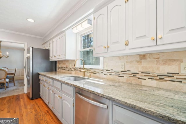 kitchen with crown molding, a sink, light stone countertops, appliances with stainless steel finishes, and white cabinets