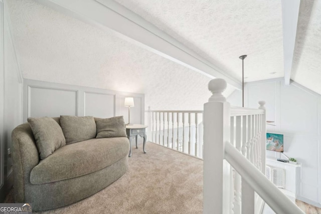 living area featuring an upstairs landing, lofted ceiling with beams, a textured ceiling, a decorative wall, and carpet