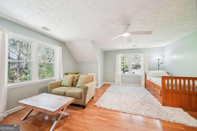 bedroom featuring a textured ceiling, visible vents, light wood-style flooring, baseboards, and vaulted ceiling