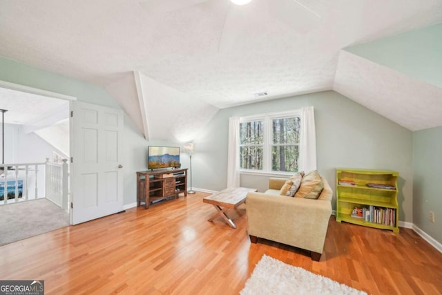 living area with vaulted ceiling, baseboards, a textured ceiling, a ceiling fan, and wood finished floors