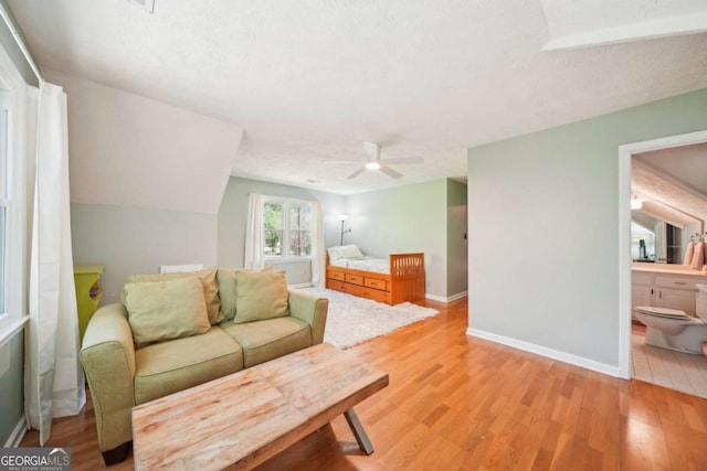 bedroom with baseboards, ceiling fan, lofted ceiling, light wood-style floors, and ensuite bath