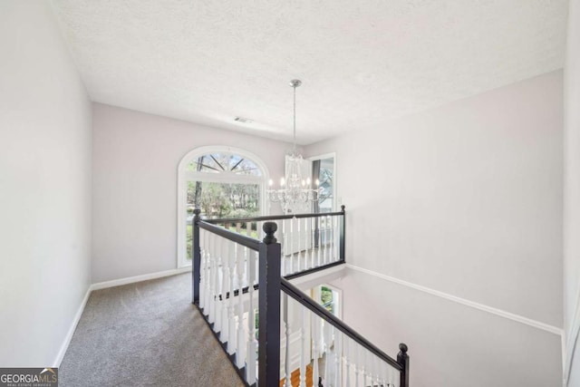 hall featuring carpet flooring, an upstairs landing, a textured ceiling, baseboards, and an inviting chandelier