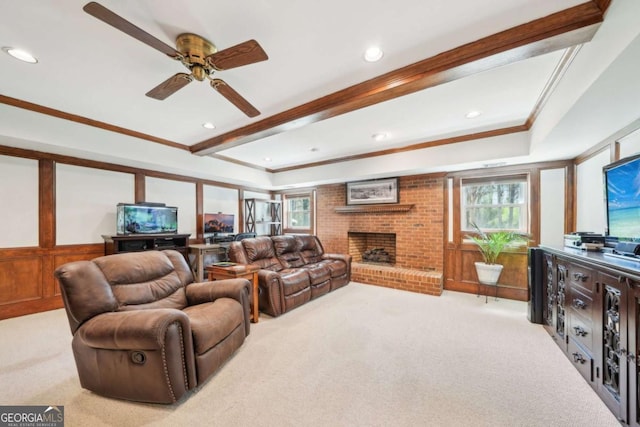living area featuring a ceiling fan, a brick fireplace, crown molding, and light colored carpet