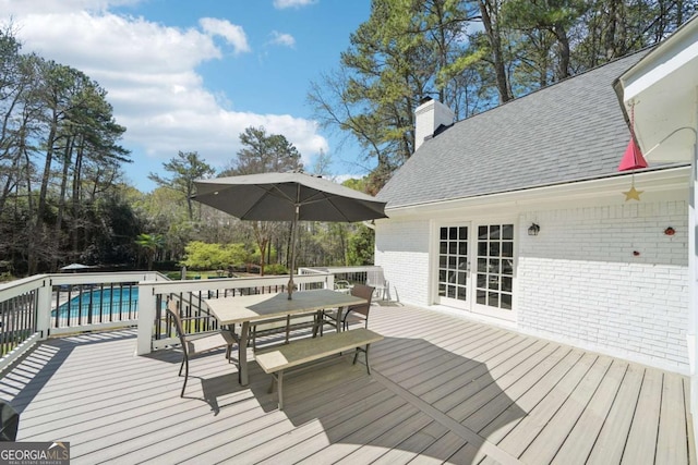 deck with outdoor dining area, an outdoor pool, and french doors