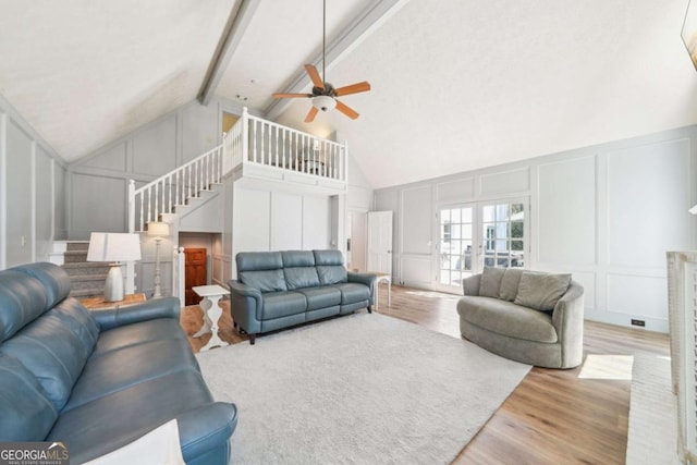 living area featuring stairs, beam ceiling, a ceiling fan, wood finished floors, and a decorative wall