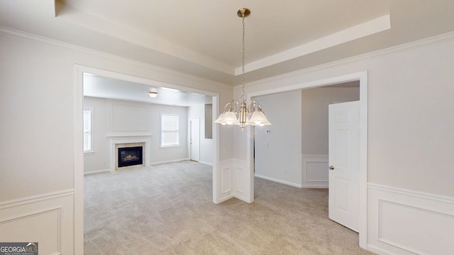 unfurnished dining area with light carpet, a tray ceiling, a notable chandelier, and crown molding