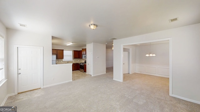 unfurnished living room with an inviting chandelier, light carpet, and visible vents