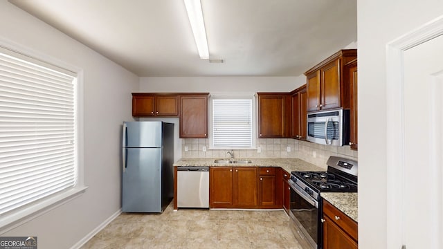 kitchen with light stone counters, a sink, backsplash, appliances with stainless steel finishes, and visible vents