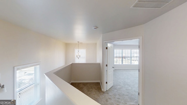 corridor with an upstairs landing, an inviting chandelier, baseboards, carpet floors, and visible vents