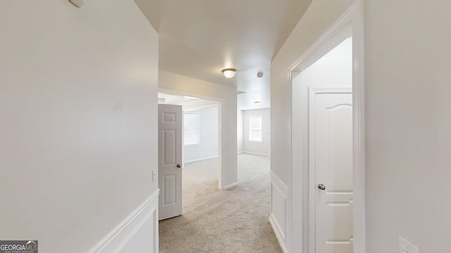corridor featuring baseboards and light colored carpet