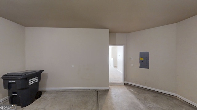 empty room with concrete flooring, baseboards, and electric panel
