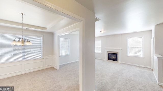 unfurnished living room with a healthy amount of sunlight, a decorative wall, carpet flooring, and an inviting chandelier