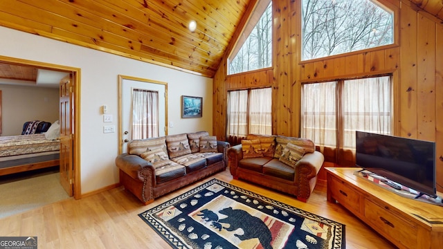 living room with baseboards, light wood-style flooring, wooden walls, and high vaulted ceiling