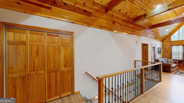 hall with an upstairs landing, lofted ceiling with beams, wood ceiling, and light wood-style floors