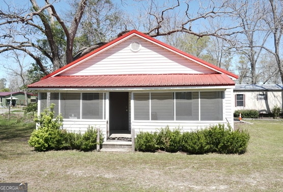 view of front of home featuring a front lawn, metal roof, and a sunroom