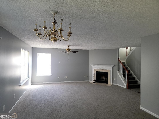 unfurnished living room with stairs, ceiling fan with notable chandelier, baseboards, carpet floors, and a fireplace
