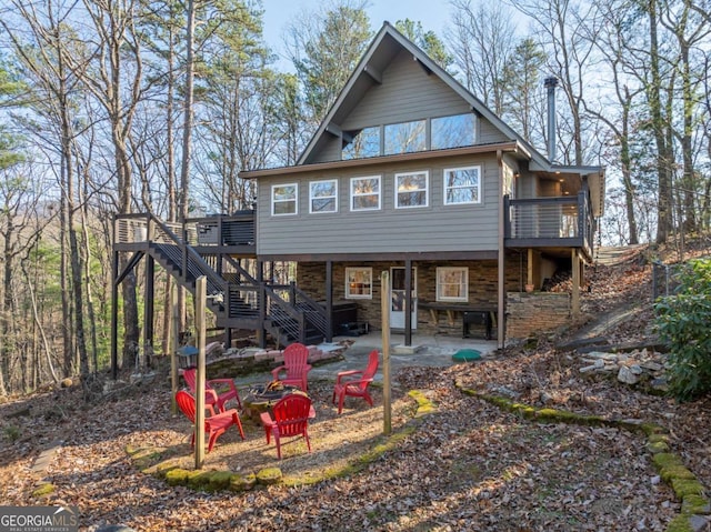 rear view of house featuring stone siding, a patio, stairway, a deck, and a fire pit
