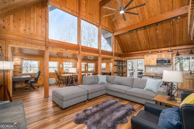living room featuring wood ceiling, a ceiling fan, wooden walls, light wood-type flooring, and beamed ceiling