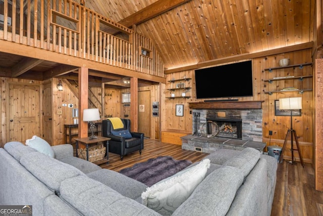 living room with wooden walls, wood finished floors, a stone fireplace, beam ceiling, and wooden ceiling